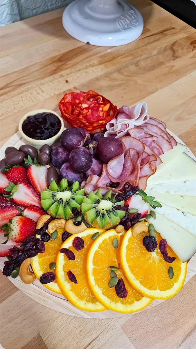Detalle de tabla de charcutería con naranjas, kiwi y quesos