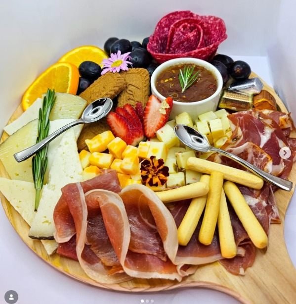 Tabla redonda de charcutería con quesos, jamón, grissini y salsa de higo