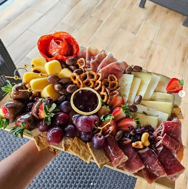 Tabla de quesos y embutidos con fresas cubiertas de chocolate, uvas y galletas saladas